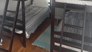 Ett rum med en våningssäng, ett fönster, trägolv och en liten matta.