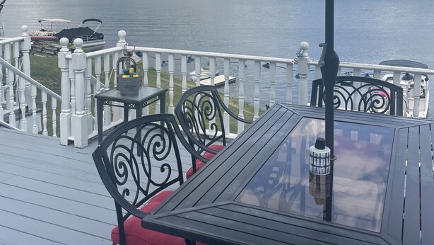 En terrass med ett bord och stolar, med utsikt över en sjö med båtar och en skogbeklädd strand.