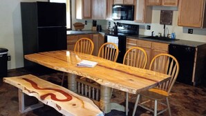 Une cuisine avec des meubles de rangement en bois, un réfrigérateur noir, un four à micro-ondes, une cuisinière et une table à manger avec des chaises.