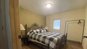 Une chambre à coucher avec un lit, deux tables de chevet, une commode, une fenêtre et une porte.