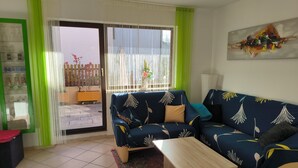 A living room with a sofa, a coffee table, and a view through a sliding glass door to an outdoor area with a fence and plants. - Beautiful 2-room granny apartment with terrace for 4 people (Burladingen)