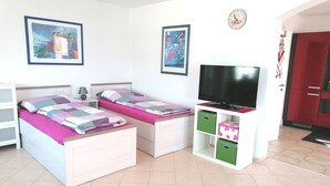 A bedroom with two beds, a TV, a clock, and storage cabinets. - Beautiful 2-room granny apartment with terrace for 4 people (Burladingen)