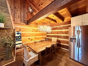 Un interior de madera con una mesa de comedor, sillas, un refrigerador y una lámpara colgante.