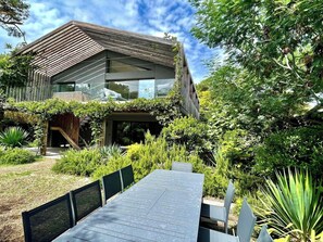 A modern house with a sloped roof, surrounded by lush greenery and a dining area with a table and chairs. - Attractive Villa with panoramic bay views A0303 (Lège-Cap-Ferret)