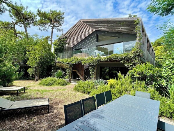 A modern house with a flat roof, large windows, and a garden with outdoor furniture. - Attractive Villa with panoramic bay views A0303 (Lège-Cap-Ferret)