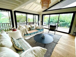 Een ruime woonkamer met een grote bank, een ronde salontafel en uitzicht op een tuin door grote ramen.