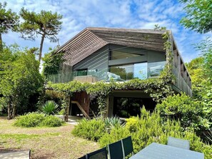 A modern house with a sloped roof, large windows, and a garden with various plants. - Attractive Villa with panoramic bay views A0303 (Lège-Cap-Ferret)