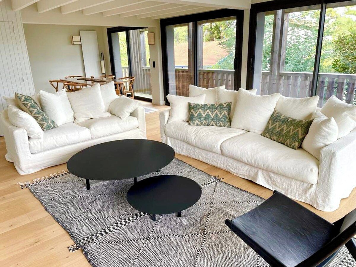 Un salon moderne avec deux canapés blancs, une table basse noire et un tapis à motifs.