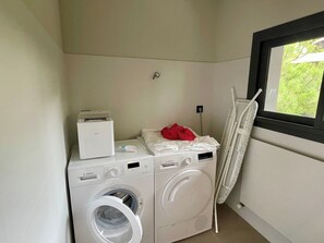 Een wasruimte met twee witte Bosch wasmachines, een rode handdoek en een droogrek.