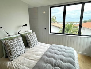 A bedroom with a large bed, two bedside lamps, and a window with a view of buildings and greenery. - Attractive Villa with panoramic bay views A0303 (Lège-Cap-Ferret)