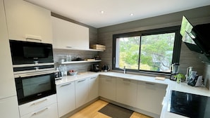 A modern kitchen with built-in appliances, a large window, and a view of greenery outside.
