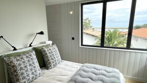 A bedroom with a large window, a bed with patterned pillows, and two bedside lamps.