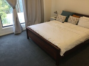 A neatly made bed with a white duvet, a wooden headboard, and a nightstand with a lamp and patterned pillows. - Unique modern, spacious, clean large 3 bedroom + study  in beautiful Blackwood (Blackwood)