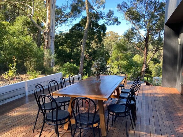An outdoor deck with a wooden table and black metal chairs, surrounded by lush greenery and trees. - Unique modern, spacious, clean large 3 bedroom + study  in beautiful Blackwood (Blackwood)