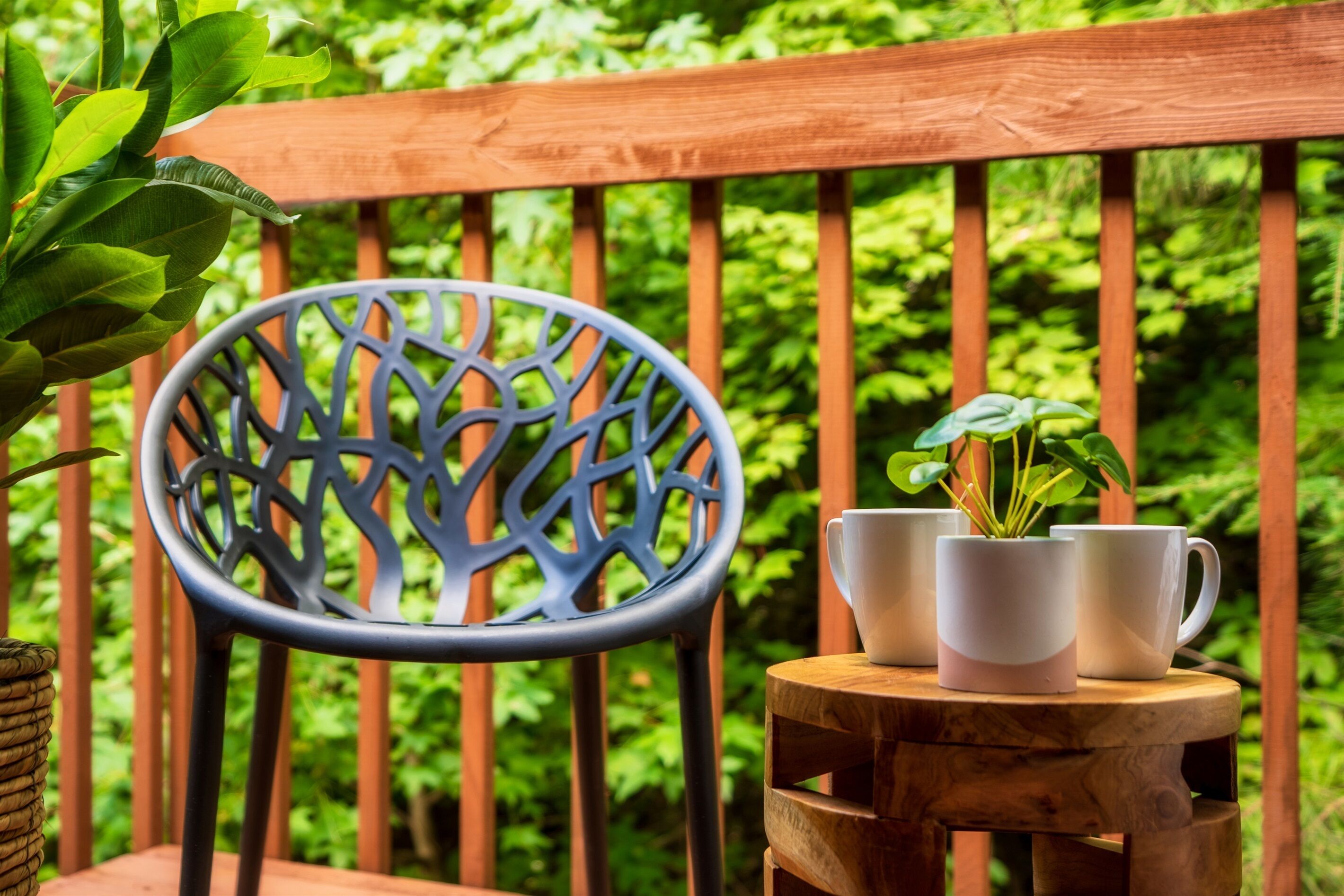 A wooden deck with a metal chair and a small wooden table holding white mugs and a potted plant.