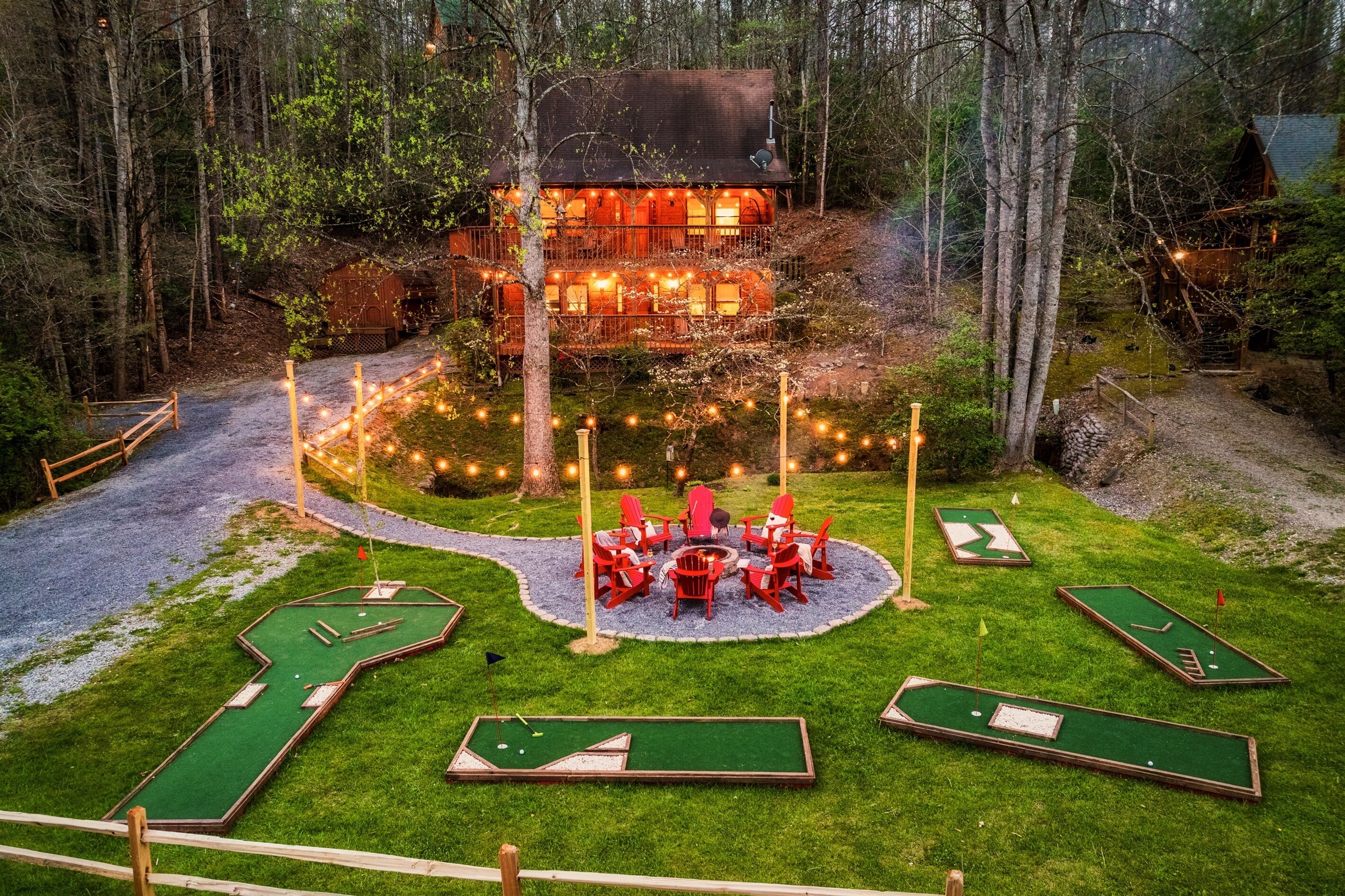 A cozy lodge surrounded by a forest, with a well-lit outdoor seating area and miniature golf holes.