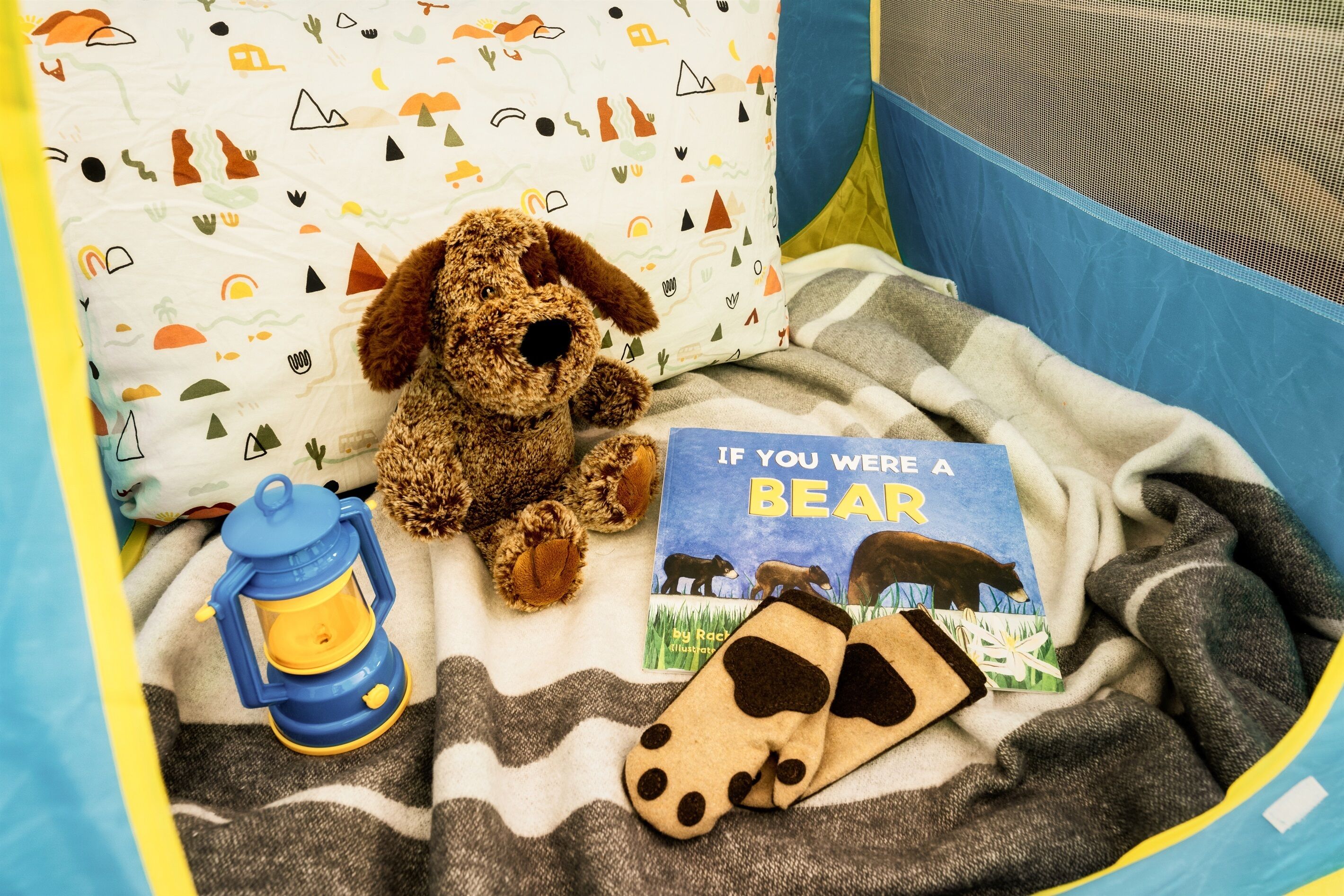 Ein gemütlicher Spielbereich mit einem Stoffhund, einem Buch mit dem Titel 'If You Were a Bear' und einer Laterne.