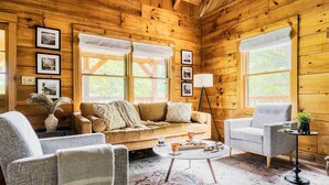 Ein gemütliches Blockhaus-Interieur mit einer Couch, Sesseln, einem Couchtisch und gerahmten Bildern an den Wänden.