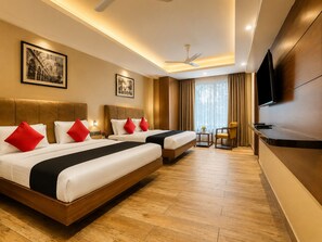 Habitación de hotel con dos camas, televisor, ventilador de techo y obras de arte en las paredes.