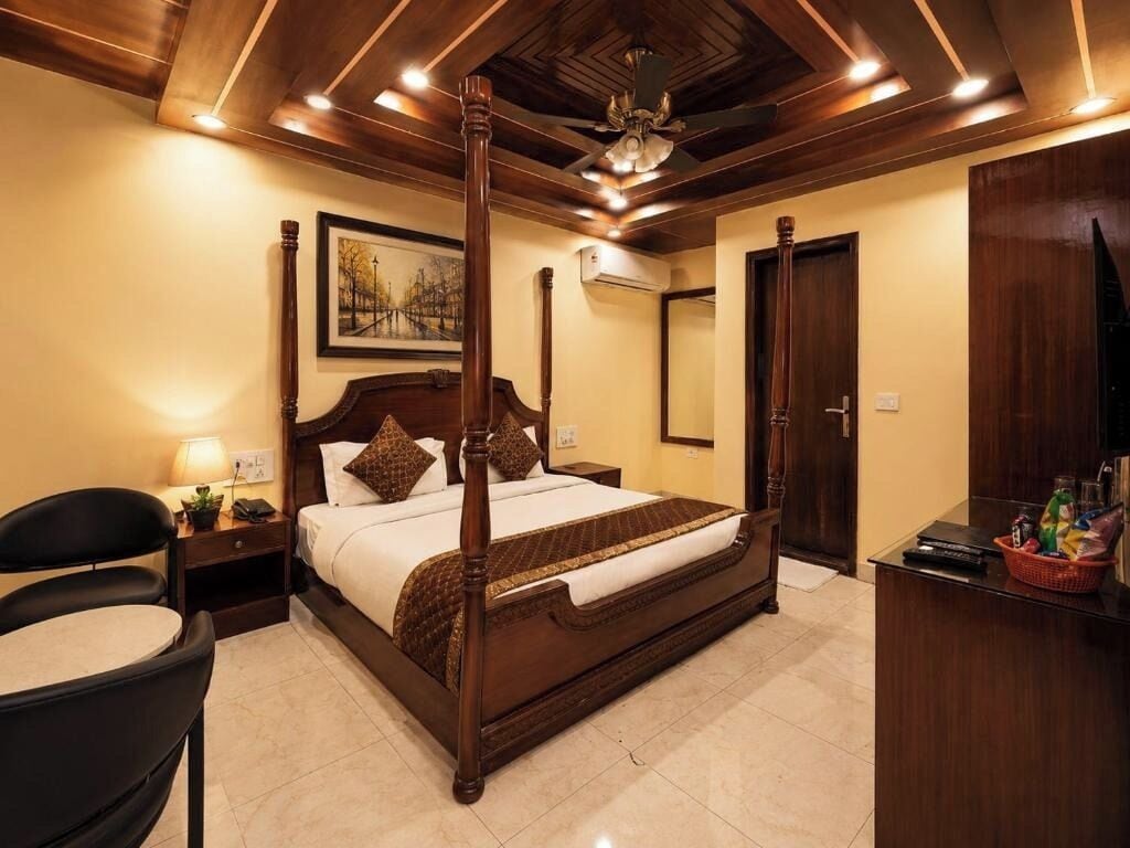 A hotel room with a four-poster bed, a desk with a chair, a nightstand, a wall-mounted air conditioner, and a door.