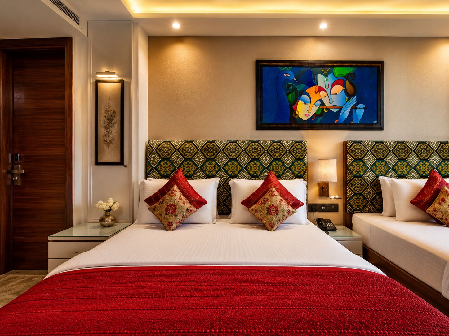Une chambre d’hôtel avec un grand lit, deux tables de chevet, une commode, un tableau au mur et une porte.