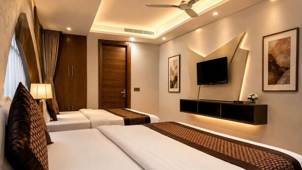 Habitación de hotel con dos camas, ventilador de techo, televisor montado y obras de arte en las paredes.