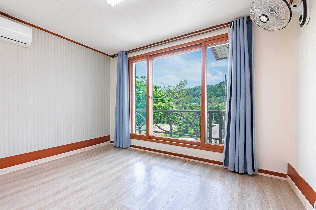 Une pièce dotée d’une grande porte-fenêtre coulissante donnant sur un balcon, d’un ventilateur de plafond et d’un climatiseur blanc.