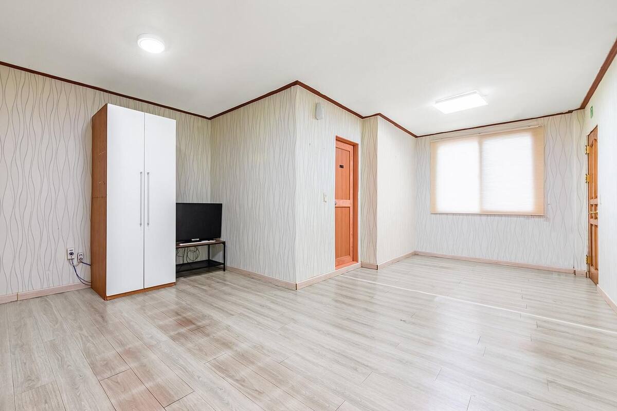 Une pièce spacieuse avec une grande armoire, un téléviseur posé sur un meuble et une porte donnant sur une autre pièce.