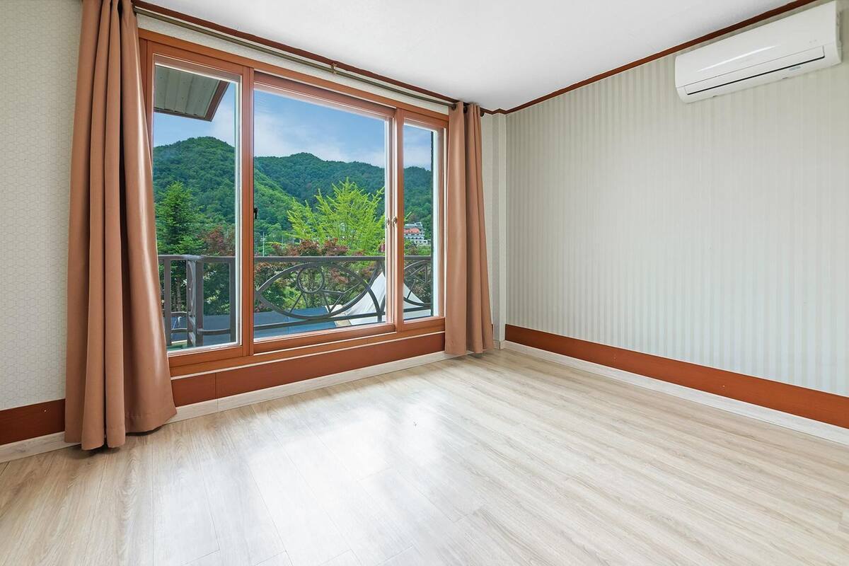 Une pièce dotée d’une grande porte-fenêtre coulissante donnant sur un balcon avec vue sur des collines verdoyantes et un ciel dégagé.