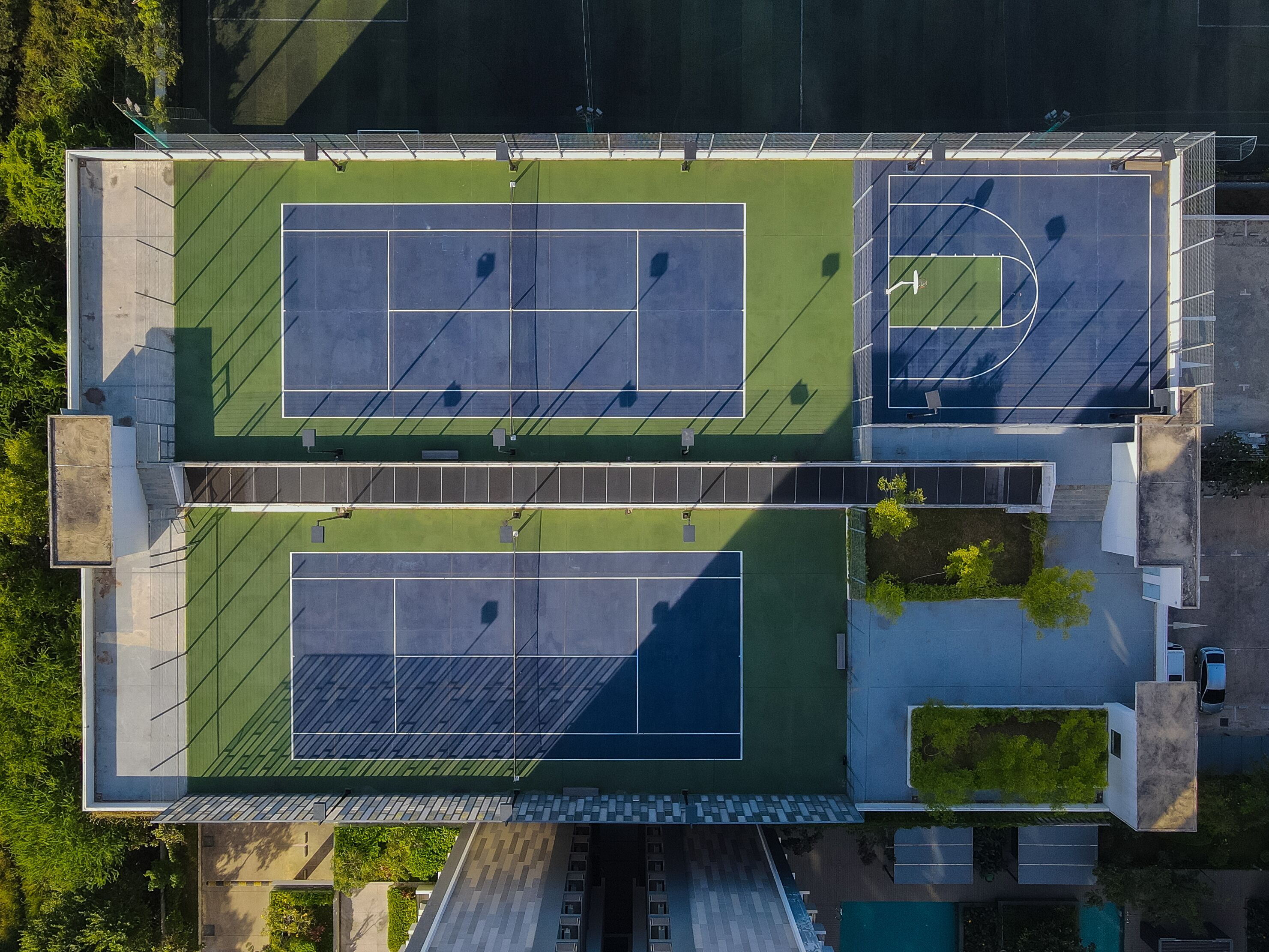 An aerial view of a tennis court complex with multiple courts, seating areas, and a parking lot.