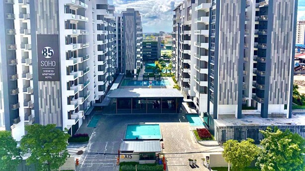 Un moderno hotel-apartamento con servicios, con varios edificios de gran altura, un área de piscina central y un patio ajardinado.