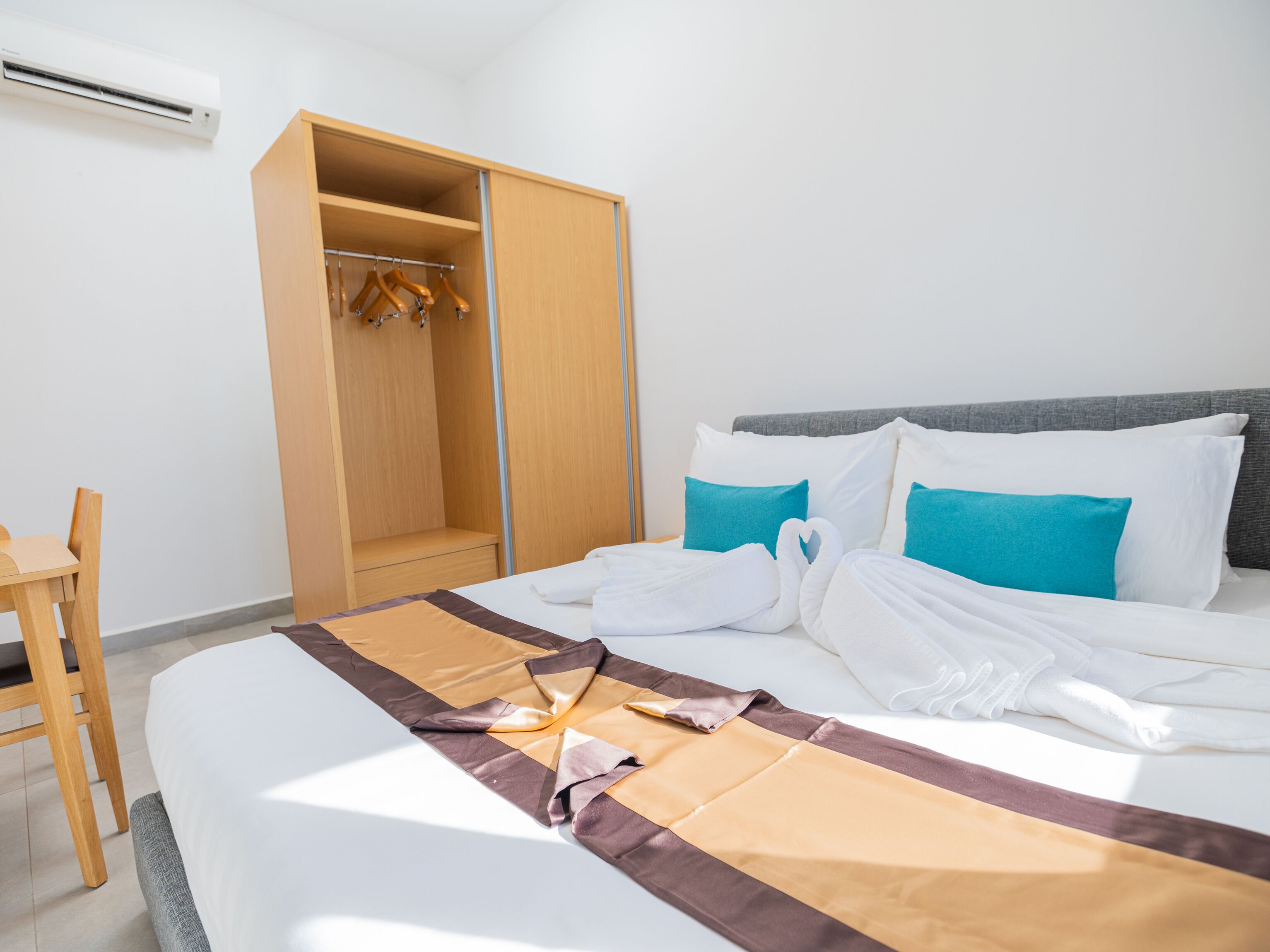 A hotel room with a bed, a wooden wardrobe, a chair, and a desk.