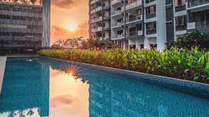 Una piscina con borde de azulejos, rodeada de follaje y edificios.