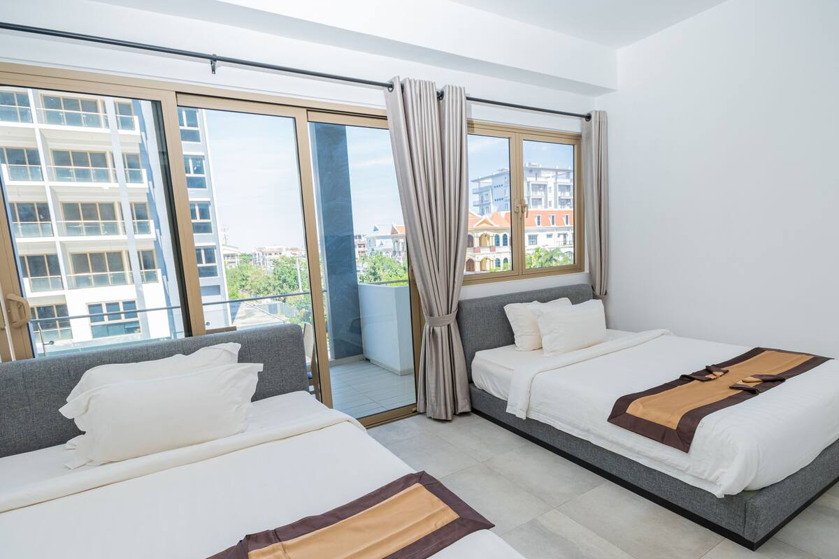 Ein Hotelzimmer mit zwei Betten, großen Fenstern und Blick auf Gebäude.