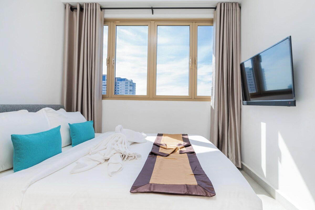 Ett hotellrum med en säng, en tv och ett fönster med gardiner.