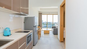 Una cocina moderna con horno empotrado, refrigerador y tetera azul. Hay un comedor con mesa y sillas, y vistas de la ciudad a través de amplios ventanales.