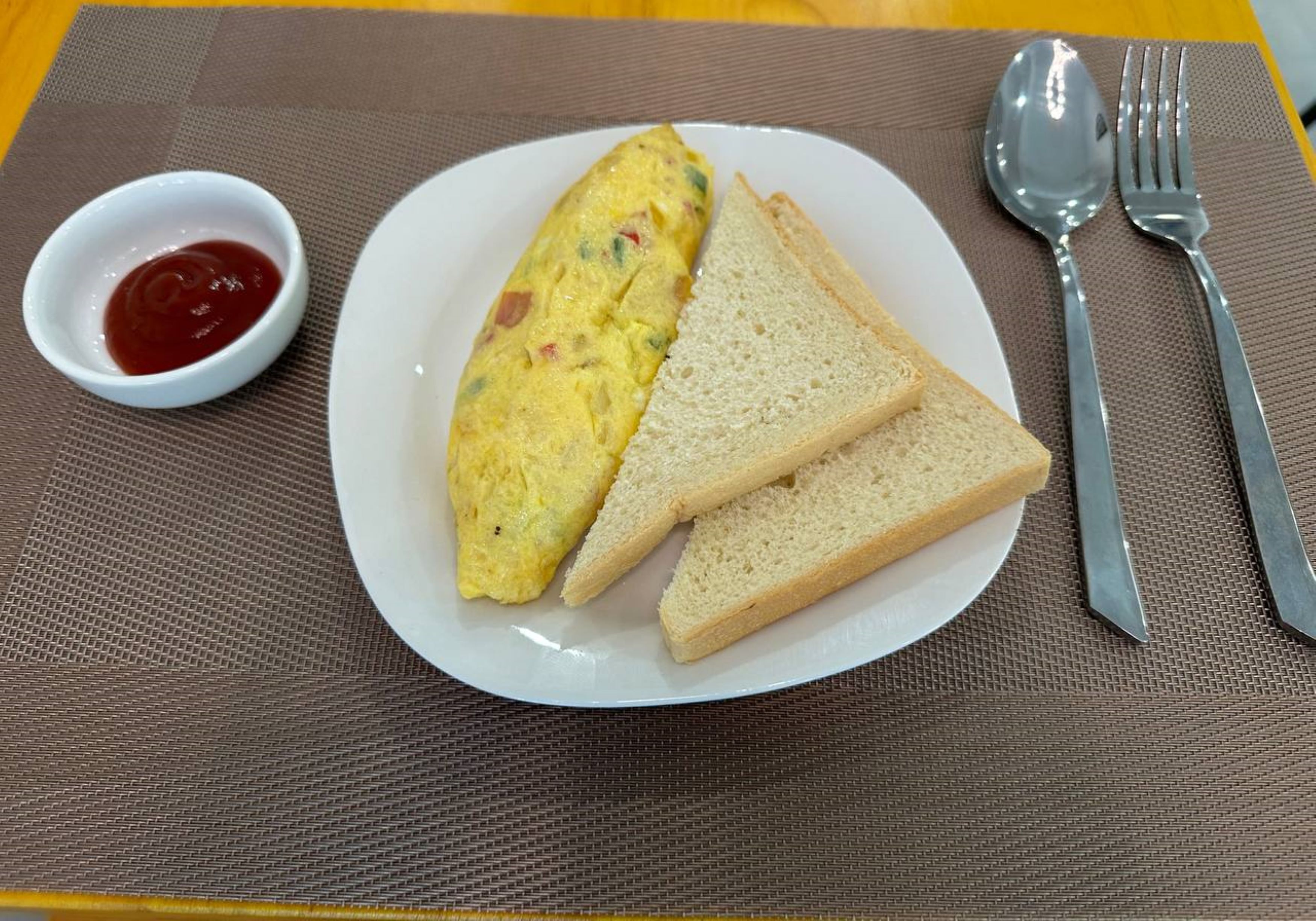 A plate with an omelet, two slices of bread, and a small bowl of ketchup.