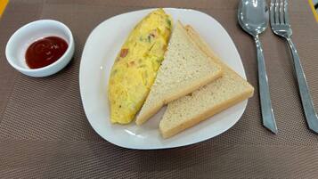 A plate with an omelet, two slices of bread, and a small bowl of ketchup.