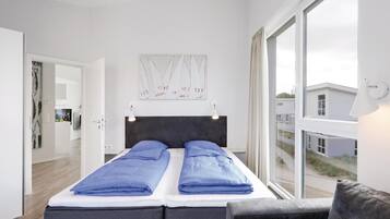 A modern bedroom with a bed, a headboard, a window, and a view of buildings outside.