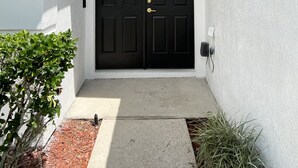 A black double door with a gold handle, white exterior walls, and a small window above the door. - New Private Pool Mid Century Modern Home Near Disney Park (Kissimmee)