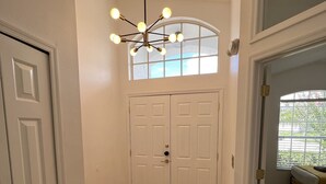 A hallway with a wooden floor, white double doors, and a ceiling light fixture. - New Private Pool Mid Century Modern Home Near Disney Park (Kissimmee)