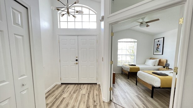 A room with a wooden floor, a bed with a yellow blanket, a ceiling fan, and a window with blinds. - New Private Pool Mid Century Modern Home Near Disney Park (Kissimmee)