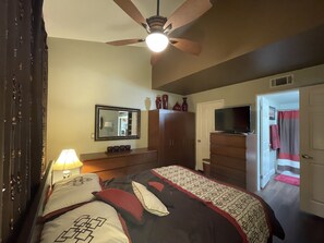 A bedroom with a bed, a ceiling fan, a TV, a wardrobe, and a door leading to a bathroom.