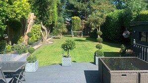 A deck with outdoor furniture, a well-maintained lawn, and a variety of trees and shrubs.