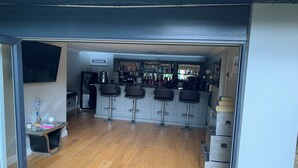 A bar area with a wooden floor, bar stools, and a refrigerator.