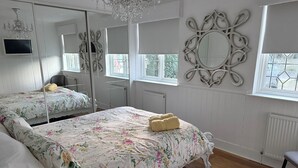 A bedroom with two beds, a chandelier, a large mirror, and a window with a view.