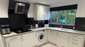A modern kitchen with a built-in washing machine, a coffee maker, and a window with a view of greenery.