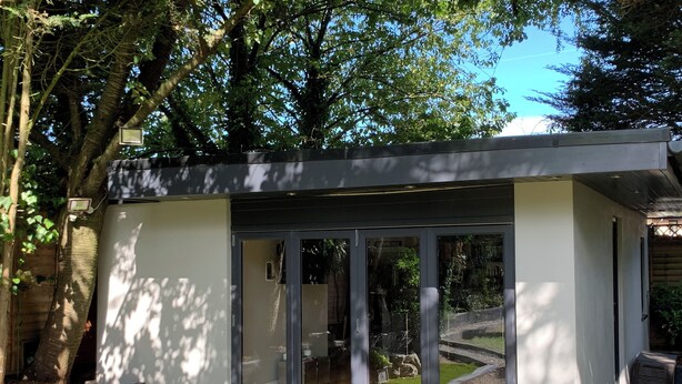 A modern, enclosed outdoor space with glass walls, surrounded by trees and a well-maintained lawn.