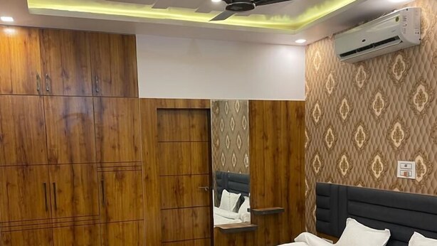 A bedroom with a bed, wooden wardrobe, ceiling fan, and an air conditioning unit. - Udiksh Hotel and Restaurants (Rohtak)