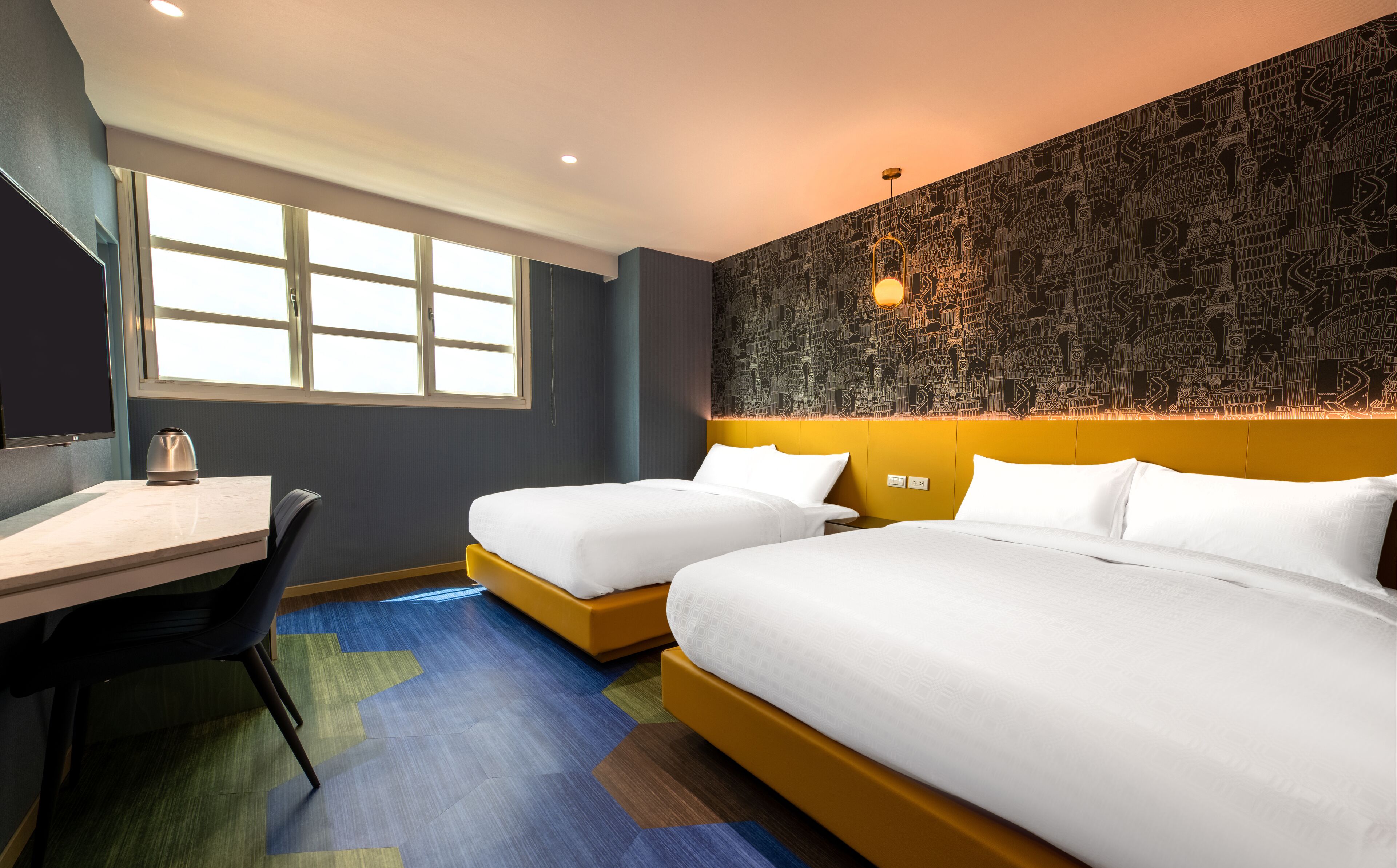 A hotel room with two beds, a desk, and a large window.